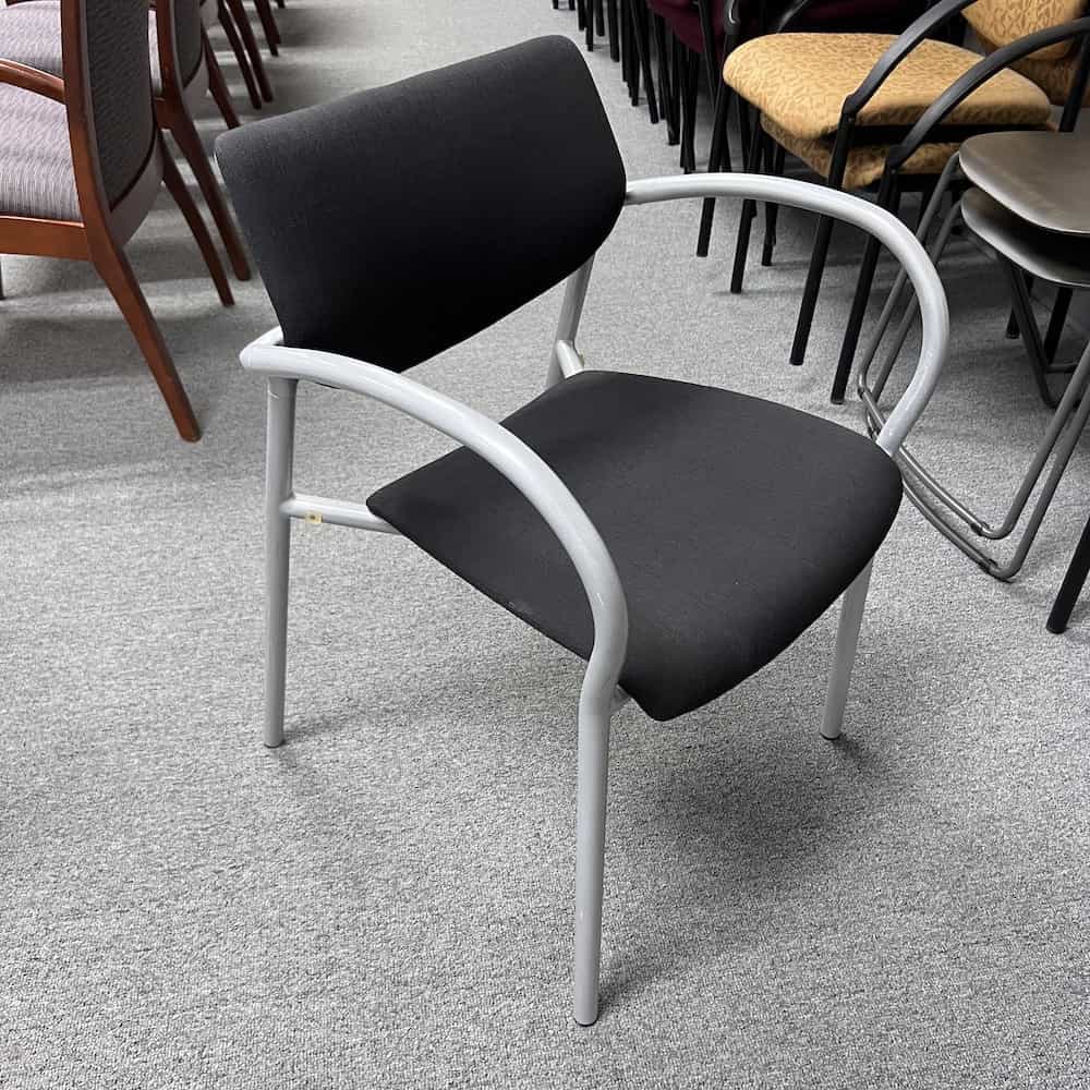 rounded arm chair with grey base and holes on back of seat and black upholstered seat, front side