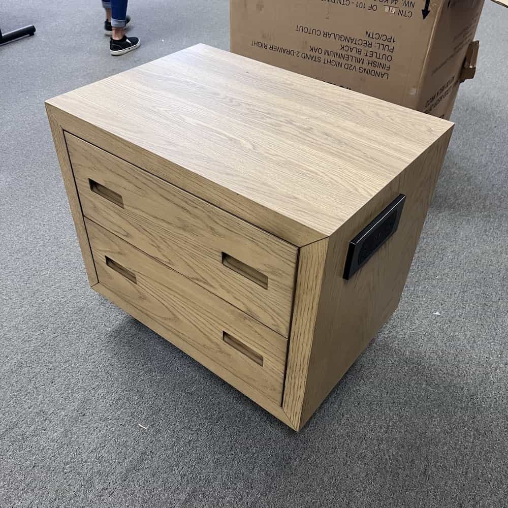 oak nightstand with two drawers with rectangle holes cut for pulls, electrical port on right side in black