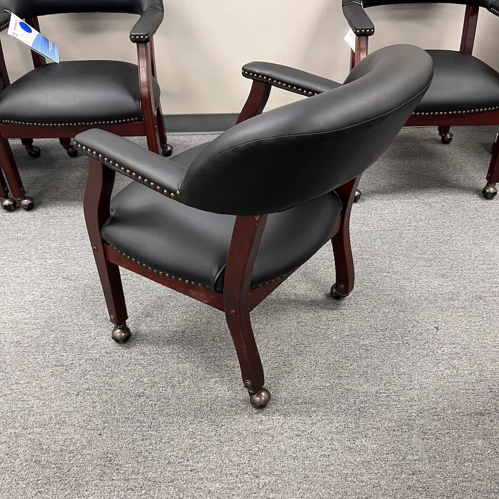 black vinyl poker guest chair with mahogany veneer wood, brass studs, and brass wheels. Office furniture seating