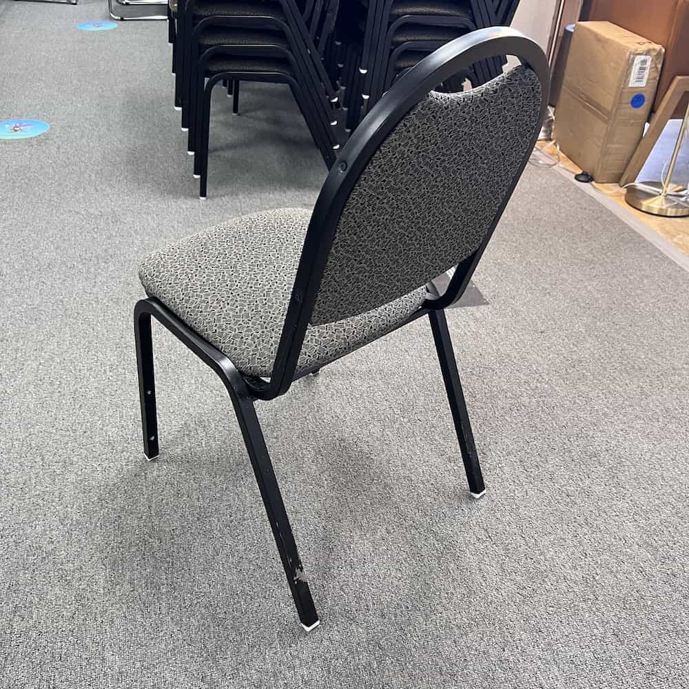 grey upholstered stacking chair with black metal base and legs, back view