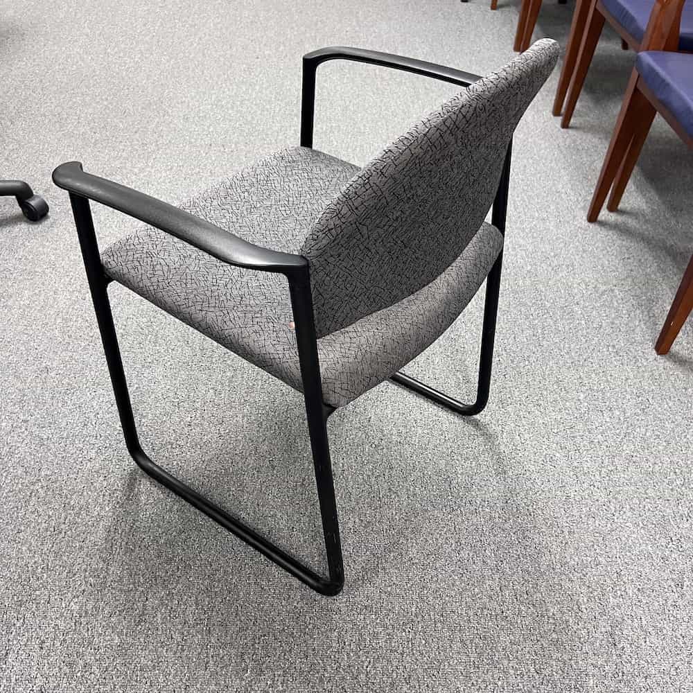 grey upholstered rounded back guest chair with black arms and legs, back