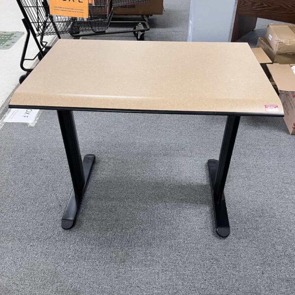 tan laminate top desk with a knife edge front, black metal T legs and black metal modestly panel