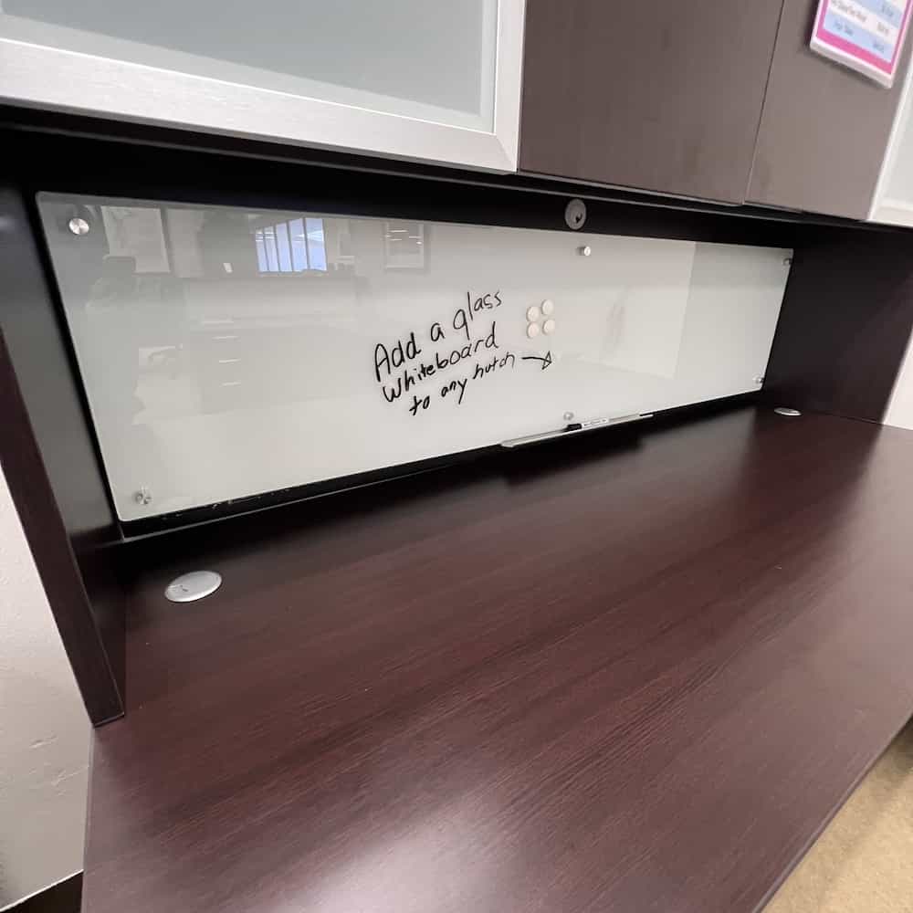 glass dry erase white board mounted on a hutch on a desk, underneath the cabinets
