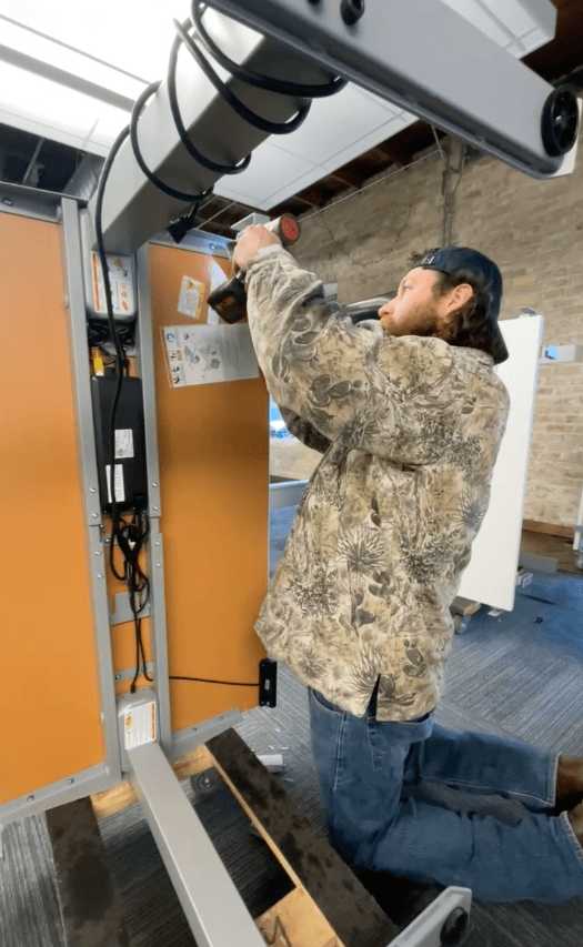 Evan using a electric tool to take apart a height adjustable desk with desk on it's side