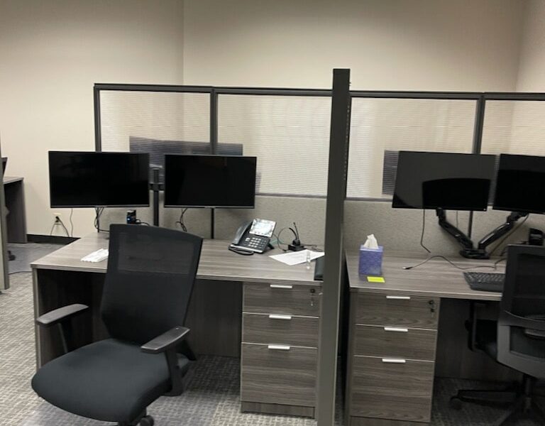 a photo showing brand new office furniture just installed, grey desks with paneling, monitor arms